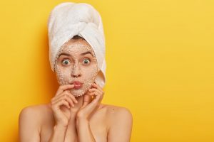 Mujer caucásica exfoliándose el rostro en fondo amarillo